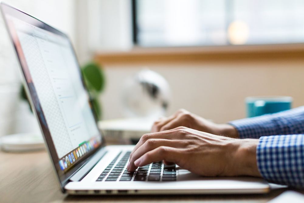 Seseorang mengetik di laptop sambil meneliti informasi di meja kerja