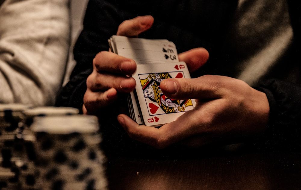 Tangan poker memegang kartu di atas tumpukan keripik taruhan
