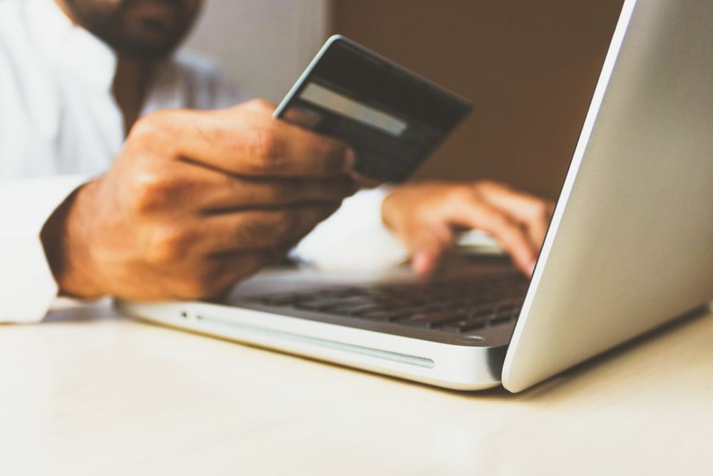 Kartu pembayaran ditahan di atas papan ketik laptop untuk transaksi digital